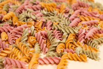 Rice vegetable pasta in the form of spirals on a white background. Healthy rice pasta with tomatoes, selenera, carrots and beets