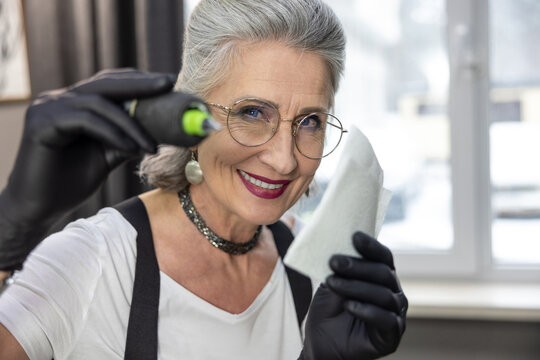 Gray-haired good-looking woman working in a tattoo salon