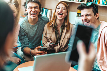 University students sitting at table with books and laptop - Millenial people studying together in library - Life style concept with guys and girls having fun in college campus