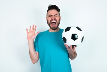 Emotive Young man holding a ball over white background laughs loudly, hears funny joke or story, raises palms with satisfaction,