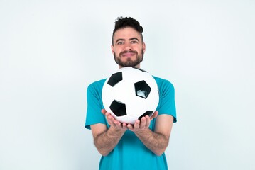 Young man holding a ball over white background holding something with open palms, offering to the camera.