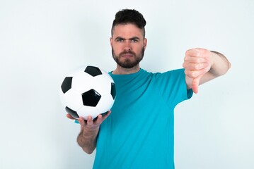 Young man holding a ball over white background being upset showing thumb down with two hands....