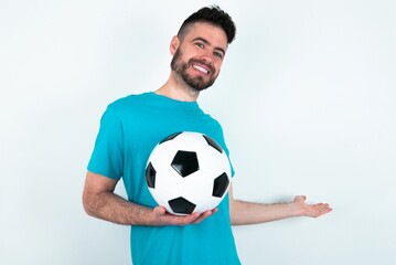 Young man holding a ball over white background feeling happy and cheerful, smiling and welcoming you, inviting you in with a friendly gesture