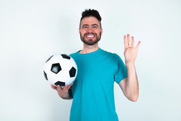 Young man holding a ball over white background showing and pointing up with fingers number four while smiling confident and happy.