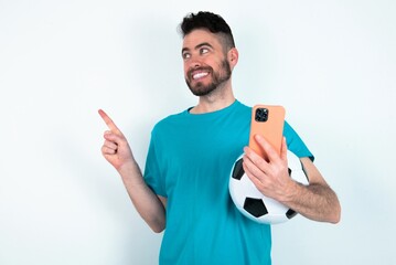 Wow!! excited Young man holding a ball over white background showing mobile phone with open hand gesture