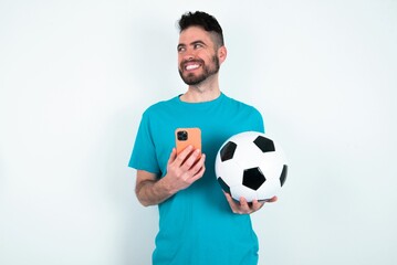 Young man holding a ball over white background hold telephone hands read good youth news look empty space advert