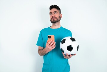 Young man holding a ball over white background holds telephone hands reads good youth news look empty space advert