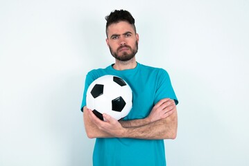 Gloomy dissatisfied Young man holding a ball over white background looks with miserable expression...