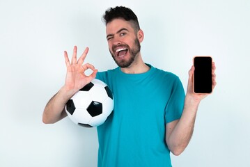 Young man holding a ball over white background holding in hands cell showing ok-sign