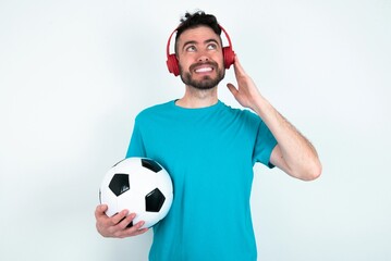 Joyful Young man holding a ball over white background sings song keeps hand near mouth as if...