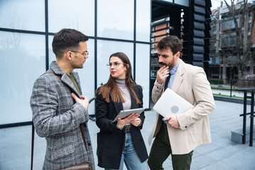 Obraz premium Group of creative business people working on social media strategy using a digital tablet. Colleagues discussing business near office building. Ideas and solutions telemarketing and telecommunication