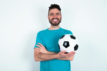 Portrait of charming Young man holding a ball over white background standing confidently smiling toothily with hands folded