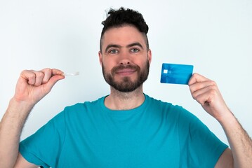 Young man holding a ball over white background holding a credit card and invisible aligner. Ready to finance treatment