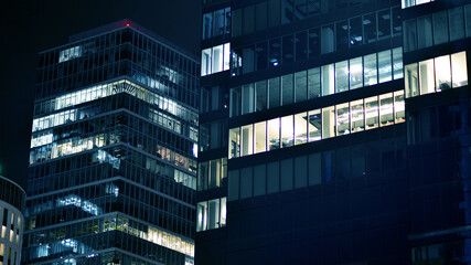 Obraz premium Pattern of office buildings windows illuminated at night. Glass architecture ,corporate building at night - business concept. Blue graphic filter.