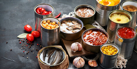 Canned vegetables, beans, fish and fruits in tin cans on black background. Food stocks.