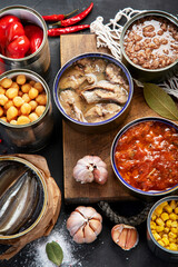 Canned vegetables, beans, fish and fruits in tin cans on black background. Food stocks.
