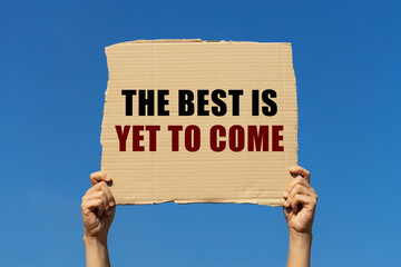 The best is yet to come text on box paper held by 2 hands with isolated blue sky background. This message board can be used as business concept about the next best thing.