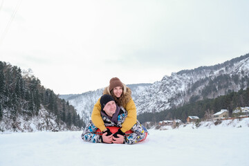 Fototapeta na wymiar Couple having fun on winter vacation, tube in snow, while spending time outdoors on snowy winter day in mountains