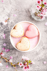 Fototapeta na wymiar Macarons or French macaroons in heart shapes with cherry blossom branch for Mothers Day