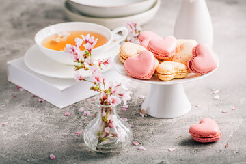 Macarons or French macaroons in heart shapes with tea with cherry blossom petals for Mothers Day