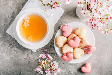 Macarons or French macaroons in heart shapes with tea with cherry blossom petals for Mothers Day