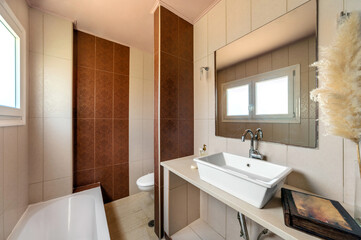 Modern bathroom design in light and beige colors. Tiled walls, white bowl sink, toilet, small window.