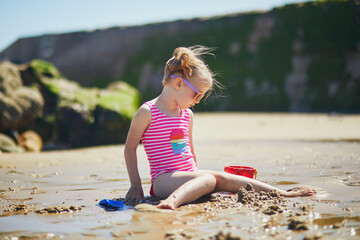 Preschooler girl playing on the sand beach at Atlantic coast of Normandy, France