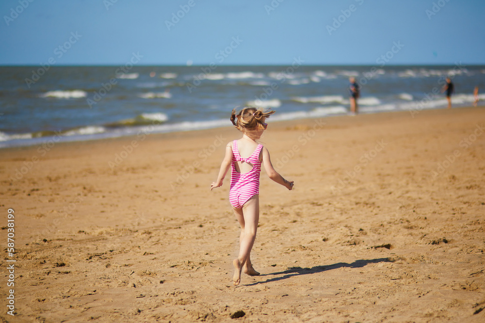 Wall mural Preschooler girl having fun on the sand beach at sea coast in Noordwijk, the Netherlands