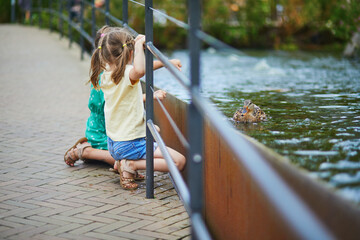Preschooler girls trying to touch ducks or fish in the water in zoo or safari park