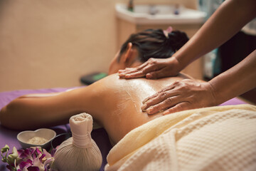 Spa therapist applying scrub salt and cream on young woman back at salon spa. Hands massaging...