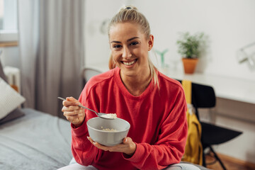 A beautiful blond woman eats oatmeal in bed