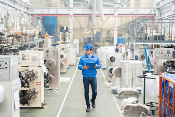 European white male engineer Was walking to explore the system in the industrial factory There are radio communications and list notes. Around there are machines working. He wore a uniform and helme