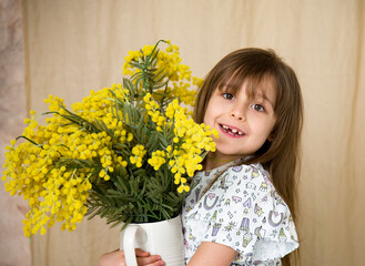smiling little brunette girl holding bouquet of yellow mimosa flowers on brown background