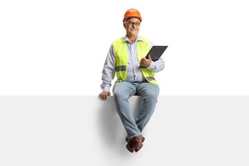 Full length portrait of a mature male engineer sitting ona blank panel and looking at camera