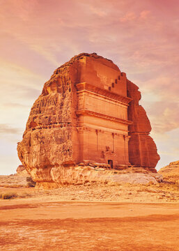 Tomb Lihyan Son of Kuza, Lonely Castle or Qasr al-Farid at Hegra, Saudia Arabia - most popular landmark in Mada'in Salih archaeological site, sandy desert landscape around - toned in orange pink color