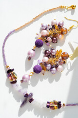 trendy author necklace with amethyst and earrings with different colors pearls around white background. fashion and handmade concept