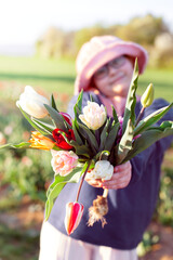 Young preteen girl stretching bunch of tulips to the camera, sunset outdoor scene. - 587053700