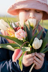 Closeup portrait of a young happy preteen girl holding a bunch of tulips and smelling the flowers