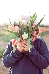 Young teenager girl hiding behind a bunch of tulips. Sunset outdoor scene, family outdoor activity time - 587054112