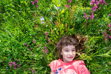 Portrait of a child girl in summer lying in the grass and wildflowers with heels and palms. summer time, freedom
