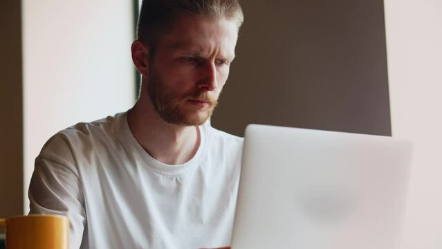 View of a young frowning programmer who is busy writing code for a mobile application. A male developer who has been working on a laptop since the morning sitting in a cafe.