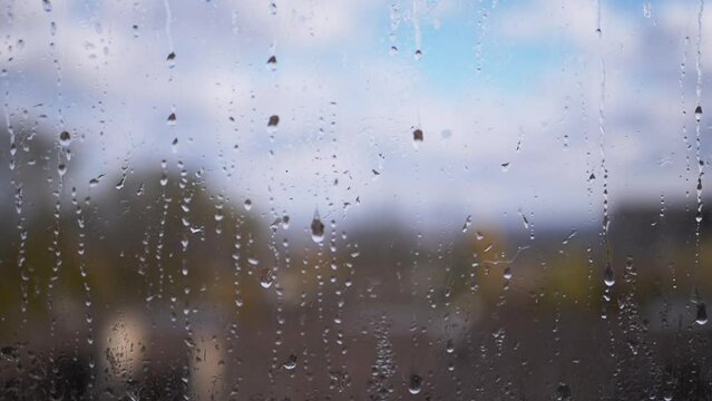Rain Drops Flow Down Glass Against a Blurred Background of Clouds, Sky, Nature. Slow-motion. Moving cumulus clouds. Rainy weather. Streams of water flow down the window on foggy glass. Meteorology.