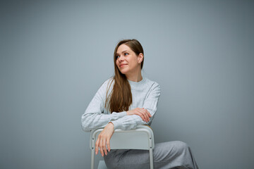 Portrait of smiling woman sitting on chair looks away.