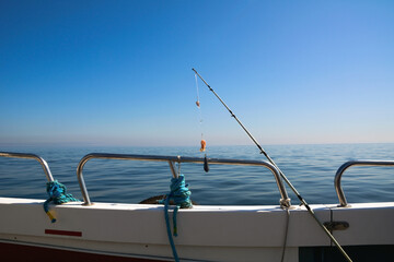 A spinning rod for catching fish is strung on the railing of a fishing boat against the background of the blue sea and sky