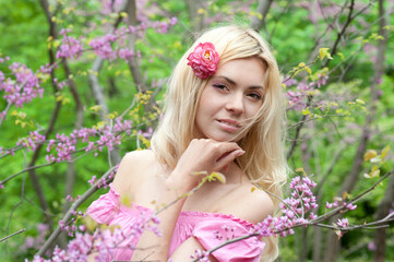 Fototapeta premium Young beautiful woman posing in blooming pink flowers spring park