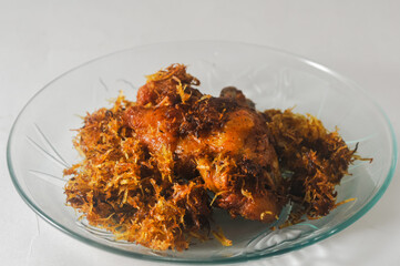 fried chicken with serundeng, which is grated coconut that is fried and seasoned, served on a small plate isolated on a white background.\