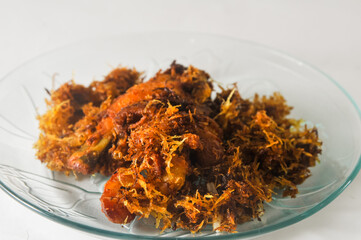 fried chicken with serundeng, which is grated coconut that is fried and seasoned, served on a small plate isolated on a white background