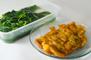 fried tempeh with flour coating served on a small plate and spinach vegetable in a transparent plastic container isolated on a white background