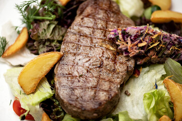 Well fried meat steak with vegetables and salad. Grilled beef steak. Baked potatoes, lettuce, cabbage and herbs for garnish. View from above. Close-up. 