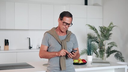 Overjoyed laughing middle aged 60s retired man in glasses looking at cellphone screen, reading message with amazing news, celebrating winning online lottery gambling auction at home